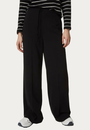Zwarte wijde broek met een koord in de taille. Gemaakt van een soepele stof, met strakke lijnen en een ontspannen pasvorm. Gekleed met witte sneakers.