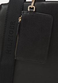 Borsa a mano nera in sintetico con superficie texturizzata, accessori in oro e portacarte rimovibile. Presenta una tracolla ampia con logo stampato.