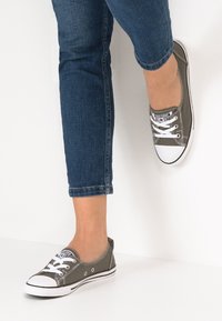Sneakers di tela grigia con suole in gomma bianca, design con lacci e cuciture a contrasto. Indossati con jeans in denim blu a vita bassa.