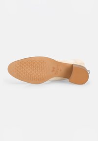 Bottine beige avec une semelle en caoutchouc texturée, un talon courbé et un design élégant. Dotée d'une fermeture éclair latérale pour un enfilage facile.