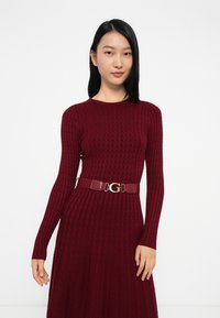 Abito in maglia bordeaux con maniche lunghe, caratterizzato da un motivo a diamante testurizzato, abbinato a una cintura lucida coordinata con una fibbia dorata con logo.