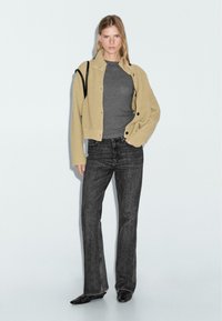 Beige ribbed cardigan, black buttons, gray fitted top, dark gray flared jeans, black heels, standing on a light background.