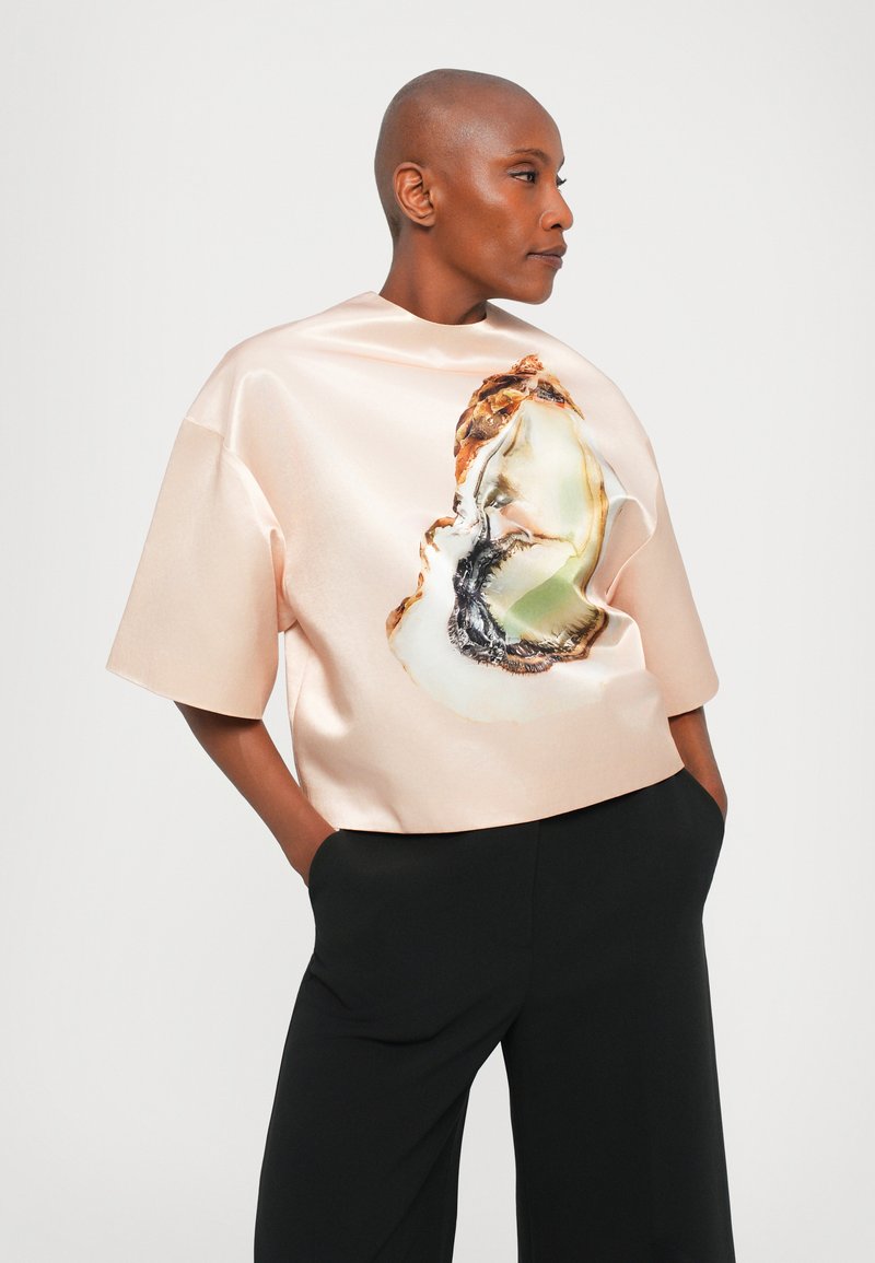 Helles rosa Satin-Oberteil mit glänzender Oberfläche, oversized geschnitten und mit einem auffälligen Austernschalen-Grafikmotiv auf der Vorderseite.
