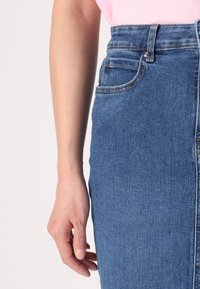 Denim skirt in dark blue, high-waisted with front pockets, visible stitching, and a smooth texture, paired with a light pink top.
