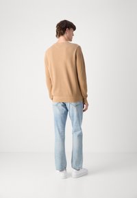 Maglione a maglia marrone chiaro con scollo a V, abbinato a jeans blu chiaro e sneaker bianche, che presenta una vestibilità comoda e polsini a costine.