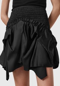 Jupe noire taille haute avec taille élastique froncée et ourlet drapé asymétrique portée par une personne avec un haut noir.