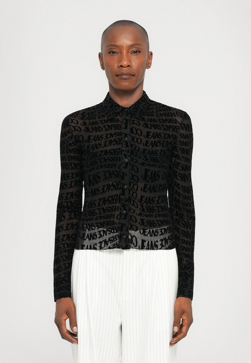 Black sheer button-up shirt featuring a textured design with repeated text patterns. Long sleeves and a pointed collar complete the look.