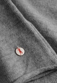 Grijze gebreide stof met een gladde textuur, met een ronde metalen tag met een rode honden-silhouet en een rode draadbevestiging.