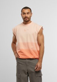 Ærmeløs gradient t-shirt i ferskennuancer, med en lysere top der falmer til en mørkere bund; har et lille broderet logo på brystet.