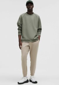 Olivengrøn sweatshirt med raglanærmer, parret med beige joggers. Hvide sneakers med sorte accenter fuldender outfittet.