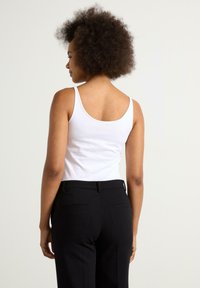 Hvid tanktop med tynde stropper, parret med sorte skræddersyede bukser. Toppen er tætsiddende, med en glat bomuldsstruktur og klassisk rund halsudskæring.