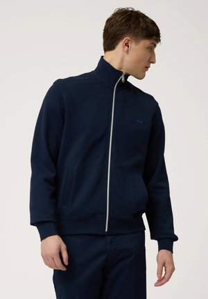 Marinblå zip-up sweatshirt med hög krage, sidfickor och en slät textur. Har en liten logotyp på bröstet och en kontrastrik dragkedja.