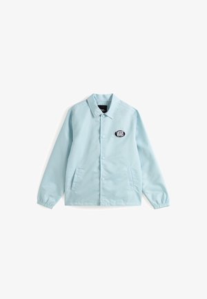 Helles blaues Jacket aus glattem Stoff, mit einem Kragen, Druckknöpfen, zwei Seitentaschen und einem schwarzen Vans-Logo-Patch auf der linken Brust.