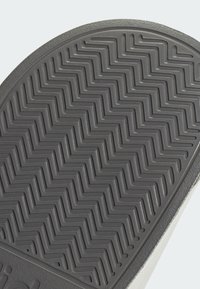 Gray rubber shoe sole featuring a zigzag texture pattern, with a smooth border edge. The design indicates durability and traction.
