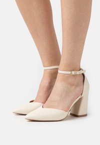 Beige korkokengät, joissa on terävä nenä ja nilkkaremmillä, leveä lohkopohja ja sileä nahka.