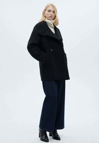 Black wool peacoat with a wide collar, double-breasted buttons, and side pockets, paired with loose blue denim jeans and black ankle boots.