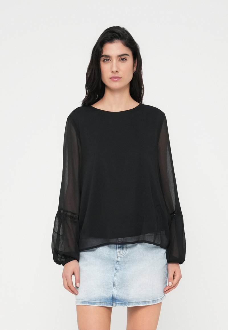 Μαύρο ημιδιάφανο μπλούζα με μακριά μανίκια, λαιμόκοψη στρογγυλή και μανσέτες με πιέτες, σε συνδυασμό με φούστα από ανοιχτό μπλε τζιν. Λεία υφή.