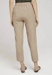 Pantalon en lin beige clair avec une taille élastiquée, design à jambes fuselées et texture lisse, présenté de dos.