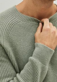 Lichtgroene geribbelde trui met een brede halslijn en gestructureerde brei. Beschikt over lange mouwen met strakke boorden. Zacht materiaal en een ontspannen pasvorm.