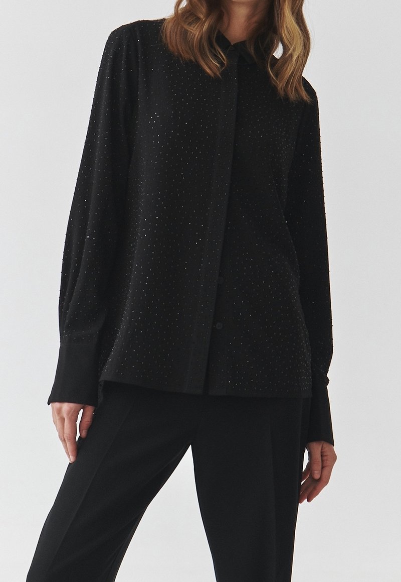 Camicia nera con bottoni, caratterizzata da una texture a pois, maniche lunghe e un tessuto morbido. Progettata con colletto classico e una vestibilità rilassata.