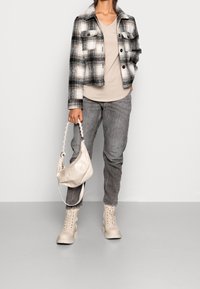 Rutig svart och vit kort jacka över en beige t-shirt, grå jeans, krämfärgade stövlar och en ljus väska med flätat handtag.