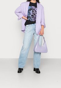 Blazer lila claro sobre una camiseta gráfica negra, combinado con jeans de tiro alto azul claro y un bolso de cocodrilo estampado en lavanda.
