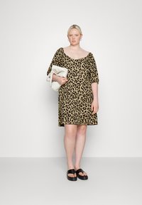 Vestido de padrão de leopardo com decote quadrado, mangas curtas balão e um corte descontraído. Usado com sandálias pretas de plataforma e segurando uma bolsa branca.