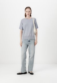 Lys blå strikket kortermet topp med rund hals, kombinert med lyse, falmede jeans og svarte ballerinatopper; modellen bærer også en liten kremfarget veske.