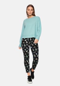 Himmelblaues, kurzes Sweatshirt mit geripptem Saum, kombiniert mit schwarzen Leggings, die mit bunten Tierillustrationen bedruckt sind. Schwarze Turnschuhe.