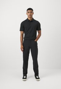 Polo negru cu mâneci scurte, cu trei butoane, asortat cu pantaloni negri. Modelul poartă adidași negri cu talpă albă.