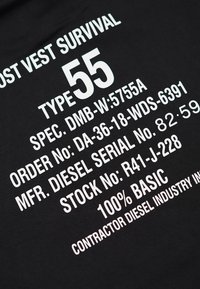 Tessuto nero con grande testo bianco che dettaglia specifiche, tipo, numeri di serie e materiale, incluso "100% BASIC."