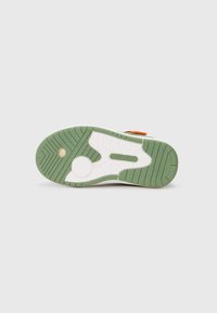 Såle av en sneakers med grønn og hvit såle, runde gripe mønstre, og "KangaROOS" logo i midten på en enkel bakgrunn.