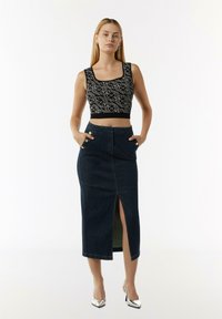 Czarny i biały wzorzysty crop top z szerokim dekoltem, zestawiony z ciemnoniebieską spódnicą dżinsową z rozcięciem z przodu i dwoma przednimi kieszeniami.