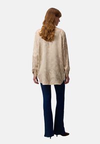 Licht beige blouse met lange mouwen en een gemarmerd patroon, gecombineerd met donkere blauwe flared jeans. Casual pasvorm, zachte stof en knoopmanchetten.
