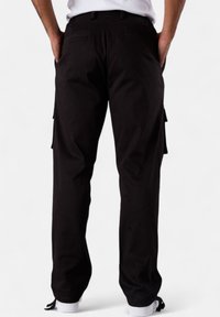 Schwarze Cargo-Hosen aus robustem Stoff, mit Seitentaschen, entspanntem Schnitt und dezenten Nähten auf der Rückseite.