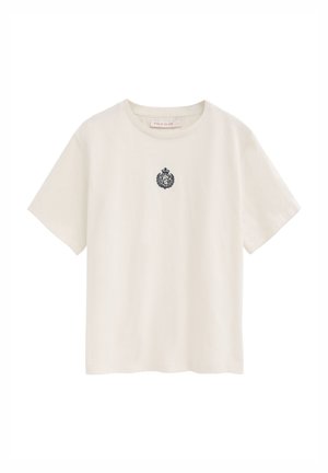 T-shirt crema a maniche corte con scollo tondo e piccolo stemma nero ricamato al centro del petto.