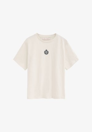 T-shirt crème à manches courtes avec col rond et petit blason noir brodé centré sur la poitrine.