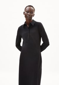 Schwarzes langärmeliges Polokleid mit Knopfleiste und klassischem Kragen. Die glatte Textur ergänzt das minimalistische Design.