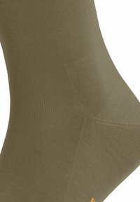 Chaussette vert olive avec une texture en côtes, dotée de coutures renforcées au niveau des orteils et d'un petit accent jaune.