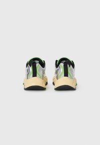 Vue arrière de chaussures de sport avec un dessus argent et noir, des accents verts, des panneaux en mesh et une semelle extérieure texturée crème. Fond en caoutchouc noir.