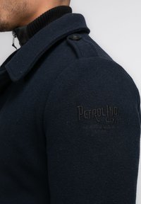 Chaqueta de mezcla de lana en color navy con hombreras, cuello de canalé negro y logotipo en relieve "Petrolind Co." en la manga izquierda.