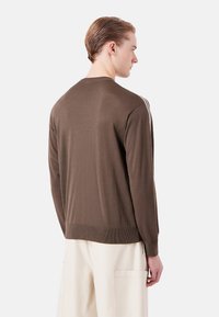 Maglione lavorato a maglia marrone con scollatura rotonda, orlo a coste e righe bianche verticali sulle spalle. Texture morbida, vestibilità casual.