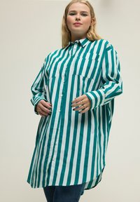 Camisa de gran tamaño a rayas verdes y blancas con botones en el frente, dos bolsillos en el pecho y mangas largas, con un dobladillo curvado.