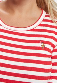 Rot-weißer gestreifter Shirt mit gerippter Textur, runder Halslinie und einer gestickten Logo auf der linken Brust.