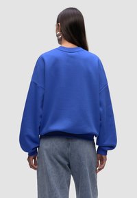 Felpa blu realizzata in materiale morbido, con una vestibilità rilassata, spalle scese e polsini a costine. Abbinata a jeans in denim chiaro.