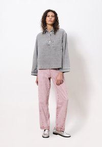 Graues Denim-Oberteil mit einem knöpfbaren Kragen, kombiniert mit hellrosa geraden Jeans und silbernen Loafers; verfügt über eine Brusttasche und ausgefranste Manschetten.