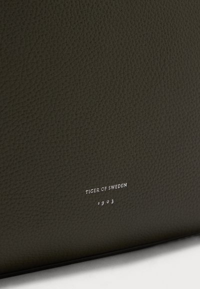 Πορτοφόλι από δερμάτινο σκοτεινό πράσινο με ανάγλυφο λογότυπο "TIGER OF SWEDEN 1903" σε ασημί, με λεία υφή και μινιμαλιστικό σχεδιασμό.