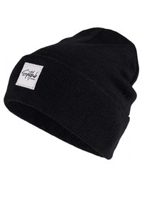 Zwarte gebreide beanie met een opgerolde rand, voorzien van een vierkant wit label aan de voorkant met gestileerde tekst, zachte textuur en klassiek ontwerp.