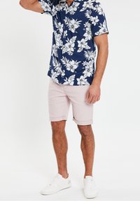 Laivastonsininen lyhythihainen paita, jossa valkoinen kukkakuosi, yhdistetty vaaleanpuneisiin shortseihin. Valkoiset tennarit täydentävät asun.