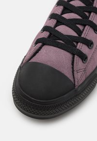 Lila mockaskor med svart gummikappa, svarta snören och strukturerad svart sula. Har stickade detaljer och rundade snörhål.